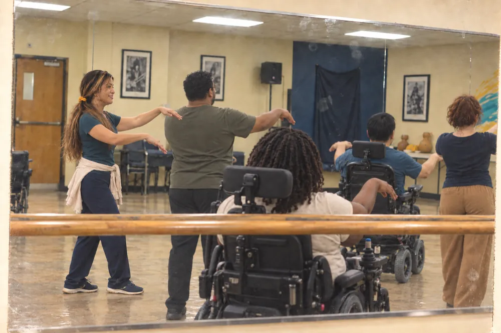In a mirror, a hula instructor leads a movement class that includes wheelchair users.