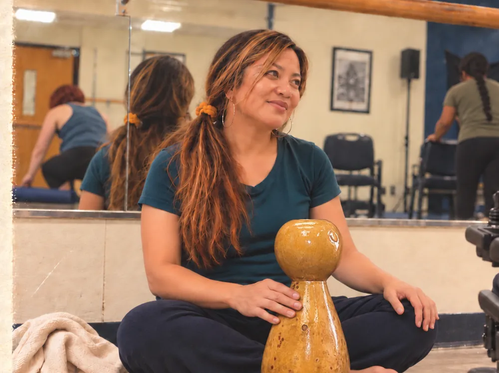 Leimomi sits with a slender amber ipu heke gourd on a mat.