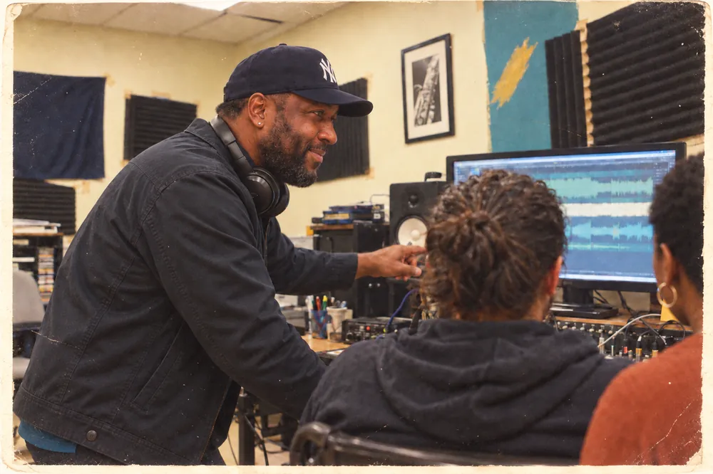 A Teaching Artist points to a waveform on a studio monitor while a student mixes.