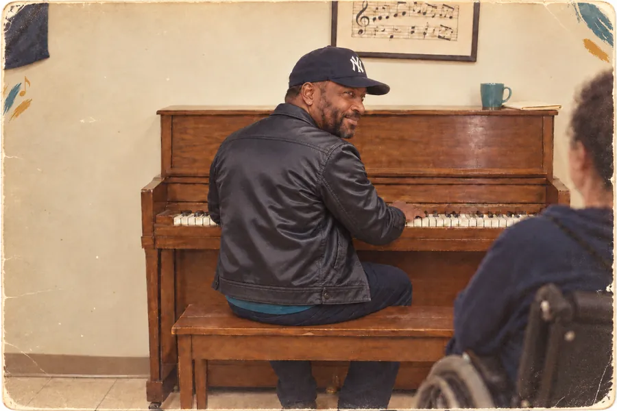A founder sits at an upright piano and glances back with a smile.